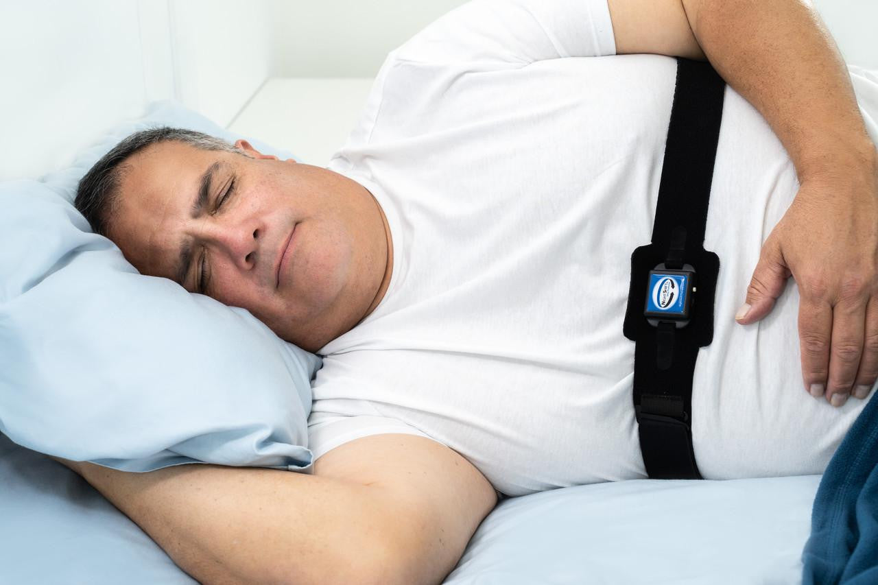 Advanced Brain Monitoring NightShift, a wearable sleep monitoring device strapped on a man's chest while he is sleeping in bed.