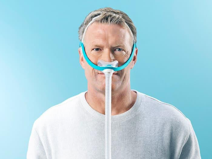 Fisher and Paykel Healthcare F&P Evora Nasal, a man wearing a nasal mask with a tube connected for respiratory support.