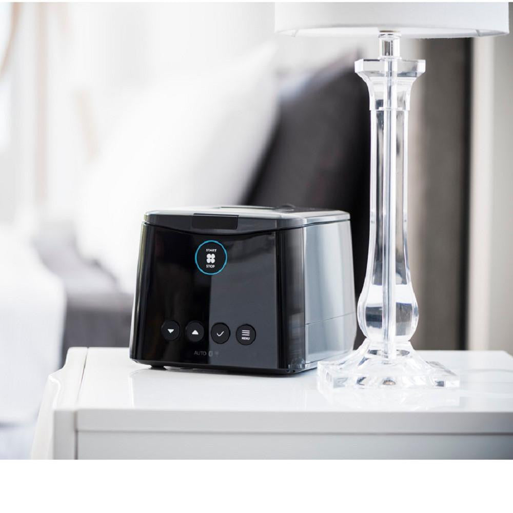 Fisher and Paykel Healthcare SleepStyle CPAP Filters, modern black device on a white bedside table with a clear glass lamp beside it.