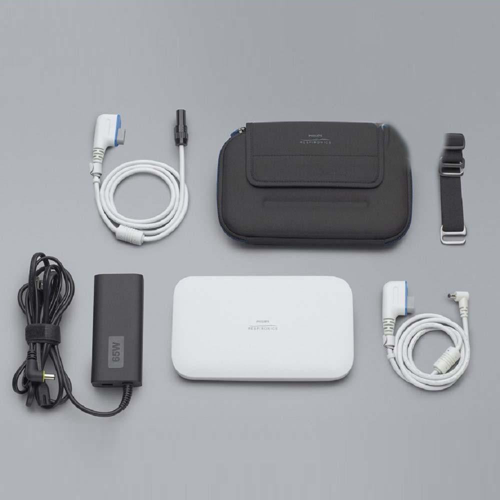 Philips Respironics CPAP Lithium Ion battery kit, image showing the kit components including a white portable battery pack, a black carrying case, a power adapter, various cables, and a strap on a gray background.