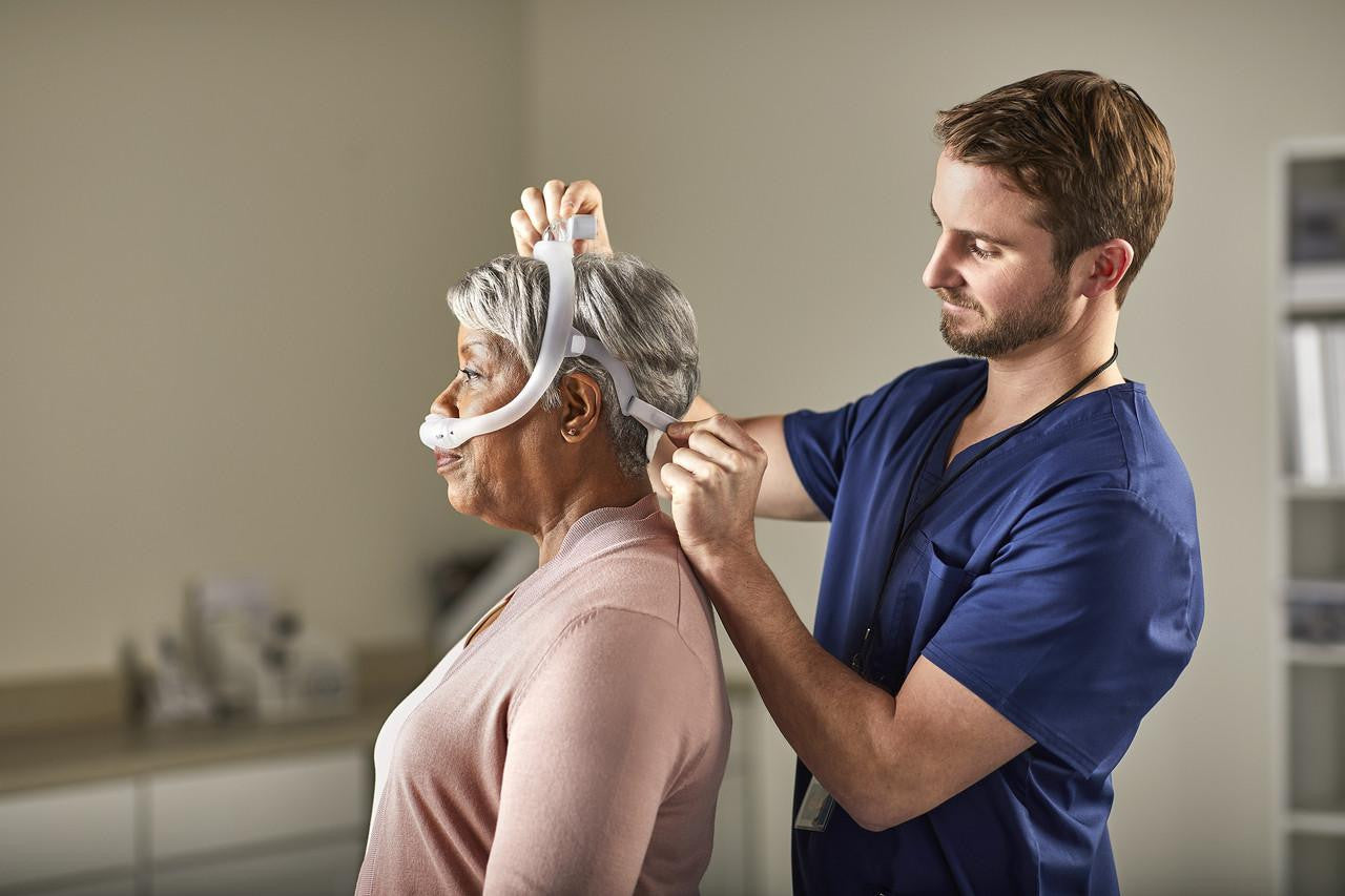 Philips Respironics DreamWear Silicone Pillows mask, showing a healthcare professional fitting the mask on an elderly woman, with two different size frames included.