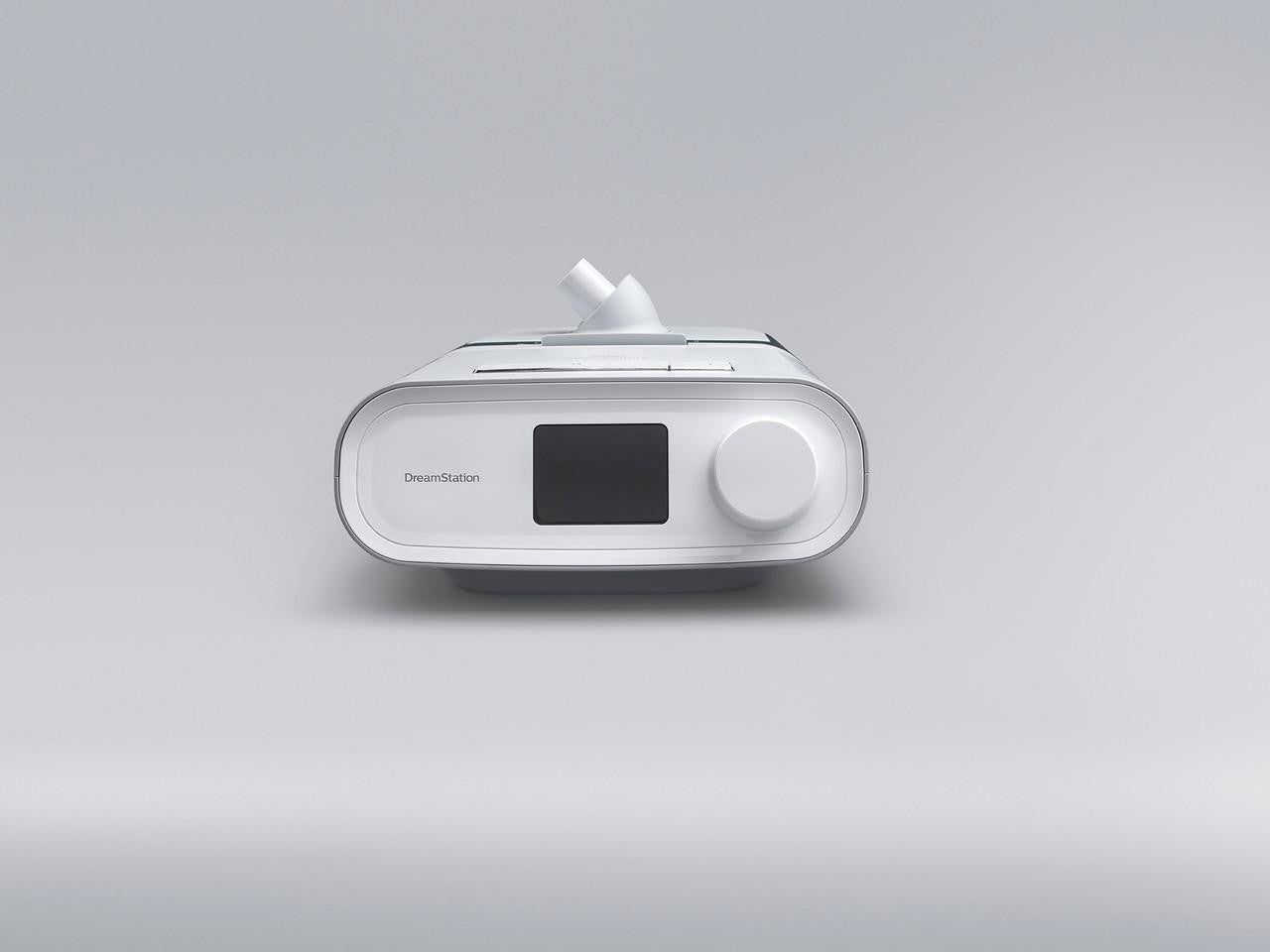 Philips Respironics DreamStation Auto + Mask Package + Modem + Bonus Accessories, white sleep apnea therapy machine with display screen and control dial on a plain gray background.