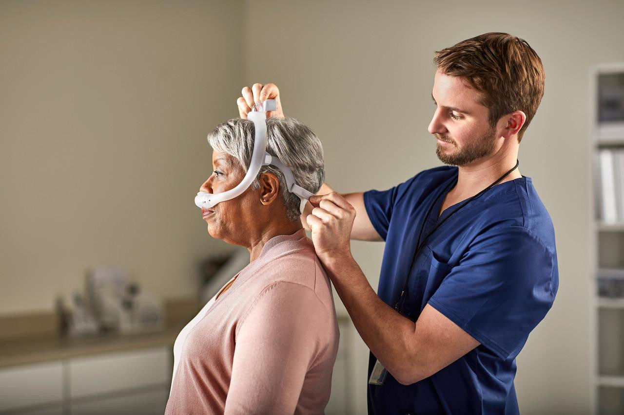 Philips Respironics Philips DreamWear Silicone Pillows CPAP mask, healthcare professional fitting elderly woman with mask in medical setting.