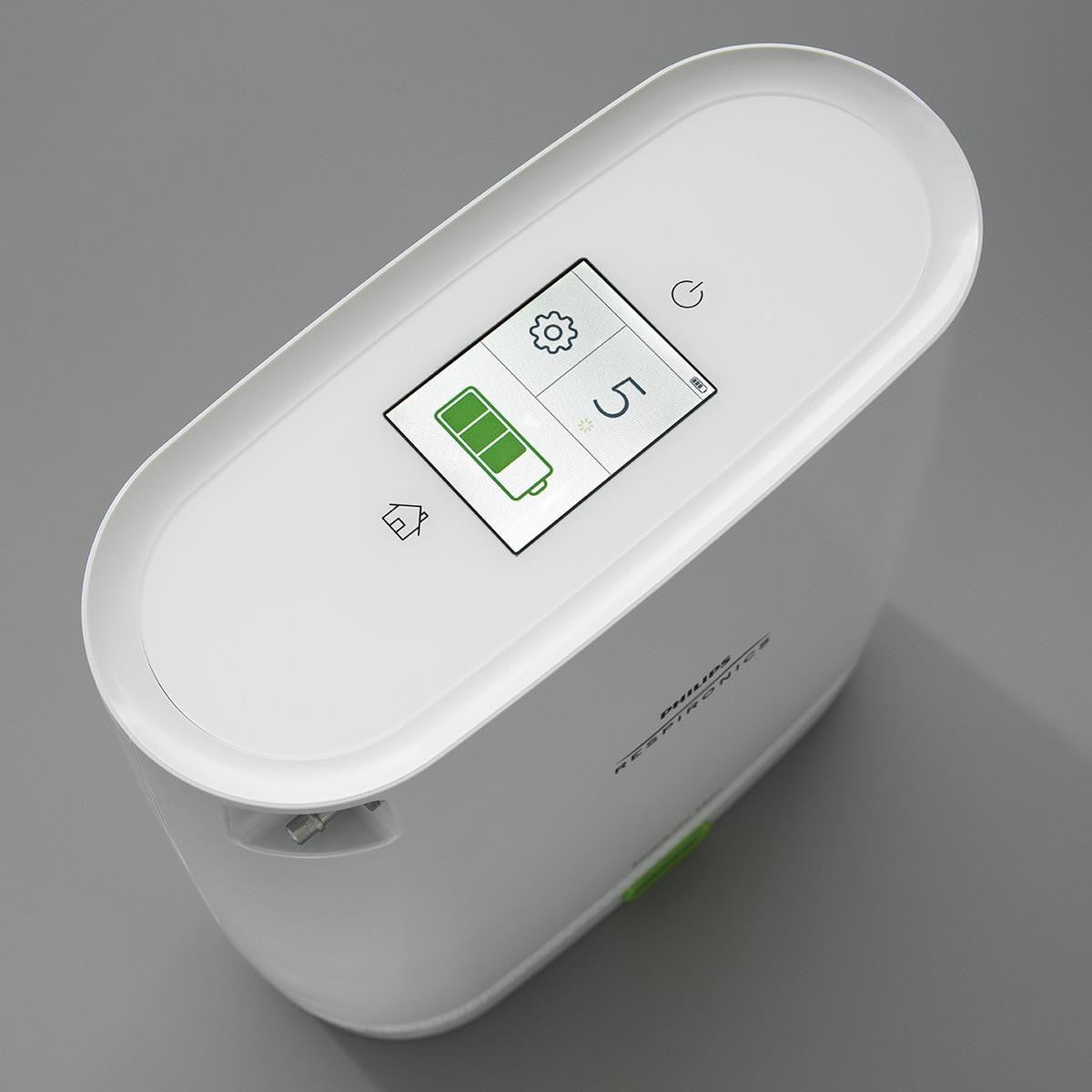 Philips Respironics Simply Go Mini Oxygen Concentrator with standard battery, digital display showing battery level, power, settings, and home icon on a white device with smooth rounded edges.