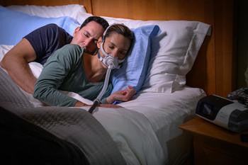 Resmed AirFit F40 Full Face CPAP Mask, a person sleeping peacefully with the mask on while resting on a bed.