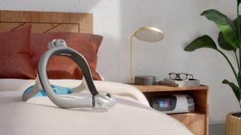 Resmed Airtouch N30i, CPAP nasal pillow mask resting on a bed with pillows and a bedside table