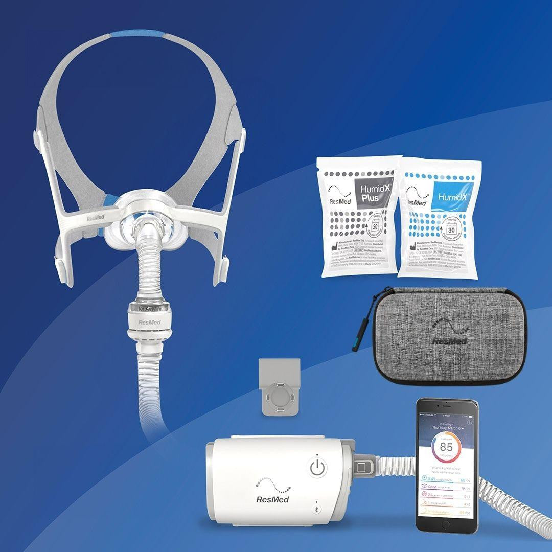 Resmed ResMed AirMini - N20 Starter kit + Deluxe Bag, including a sleep apnea mask, humidification packets, a grey carrying case, a power supply with connected tubing, and a mobile app displayed on a smartphone.