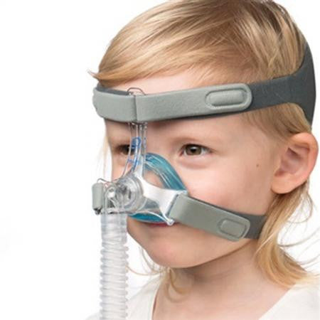 Sleepnet MiniMe 2 pediatric Nasal Mask, a small transparent nasal mask fitted on a young child with a head strap and connected to a breathing tube.